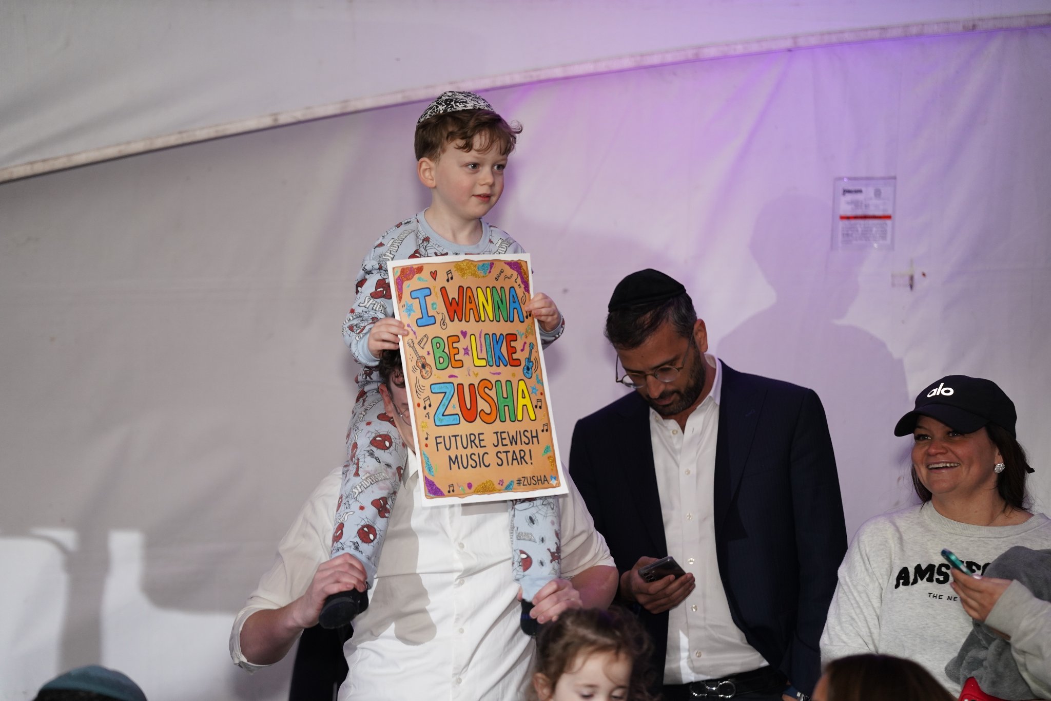 Child holding I Wanna Be Like Zusha sign at the Pesach Time Tours concert